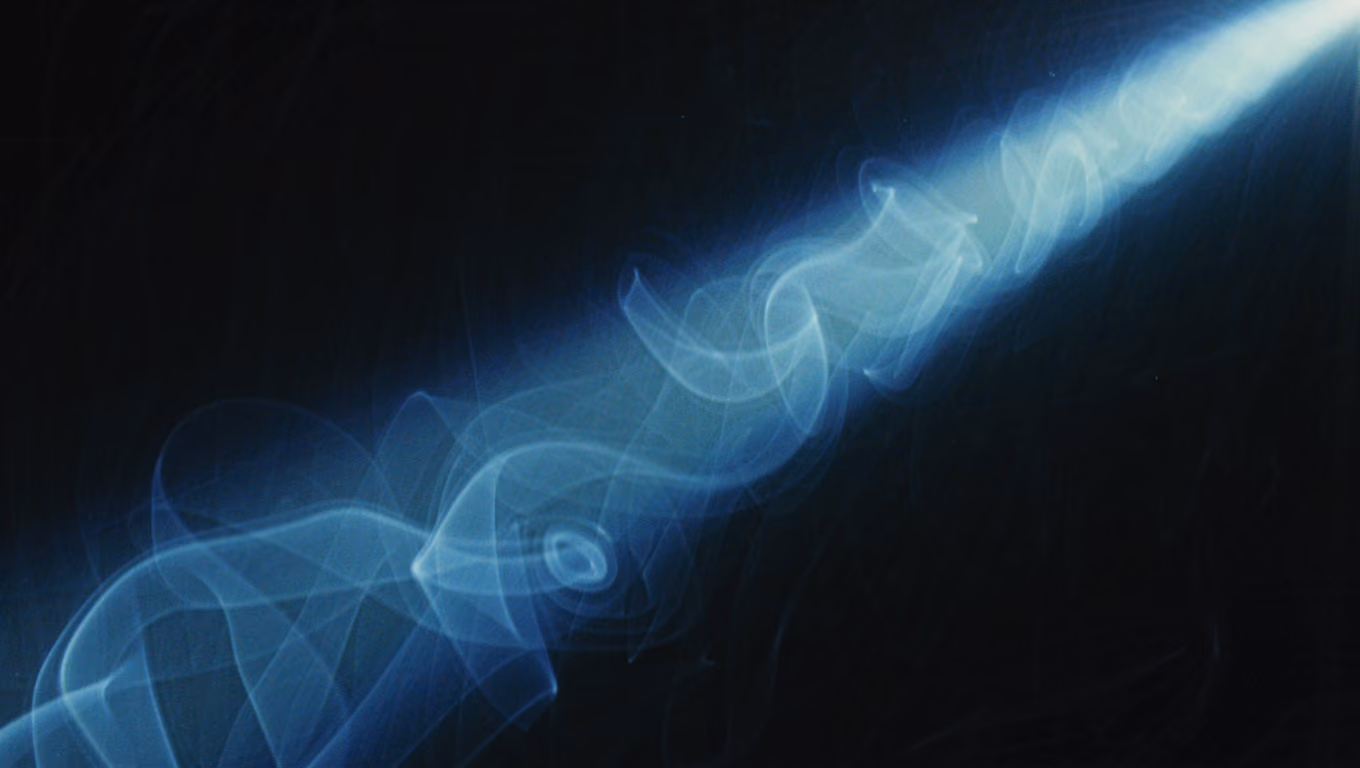 Graded still from Neón Austral: a cold cyan beam of light cutting through smoke in darkness.